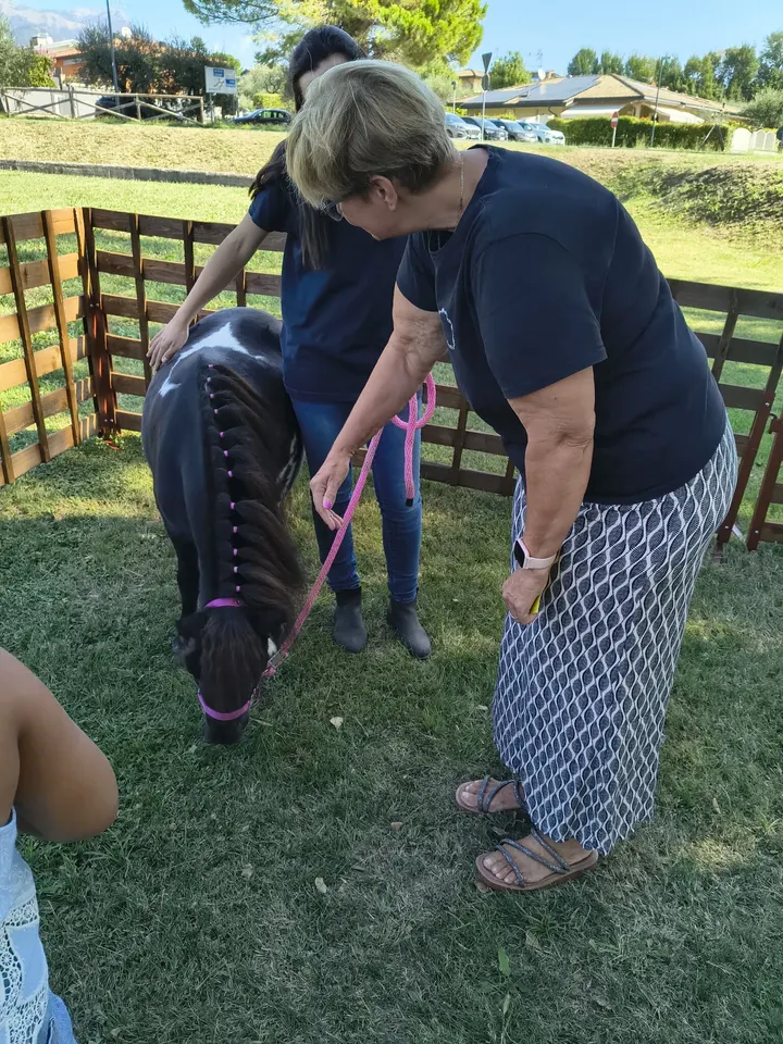Una visitatrice accarezza un piccolo pony guidato da un’operatrice