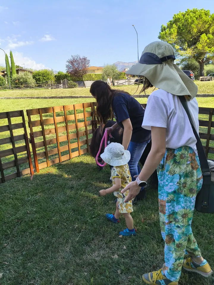 Una bambina si avvicina al pony insieme alla famiglia e a un’operatrice
